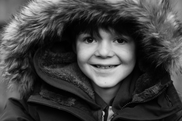 A boy smiles wearing a fur hood.