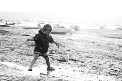 A boy splashes on beach with a boat in the background.