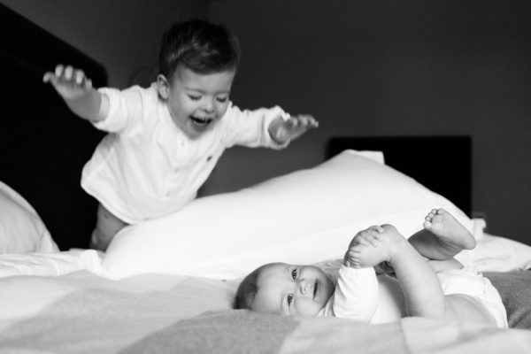 Brother leaps onto bed near baby.