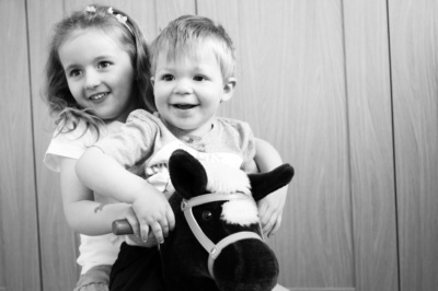 A brother and sister play on a toy horse.