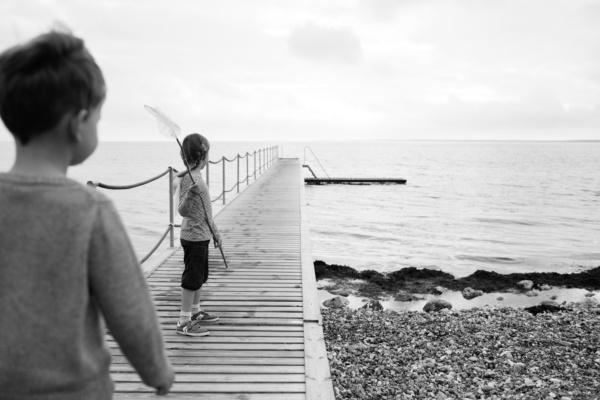 A brother and sister play on a sea jetty.