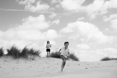 A brother and sister run down sand dunes.