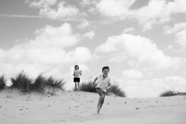 A brother and sister run down sand dunes.