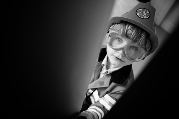 A child dresses up as a fireman and looks through an open cupboard.