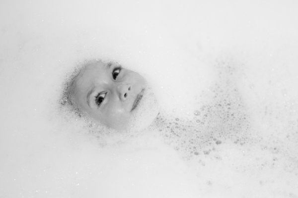 A child's face peers out of a bubble bath.