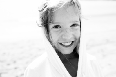 A child in a hoody smiles on the beach.