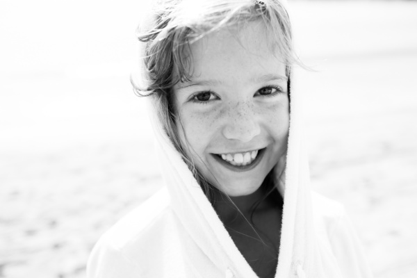 A child in a hoody smiles on the beach.