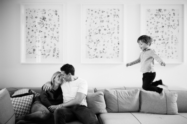 A child jumps on a sofa while their parents hug.