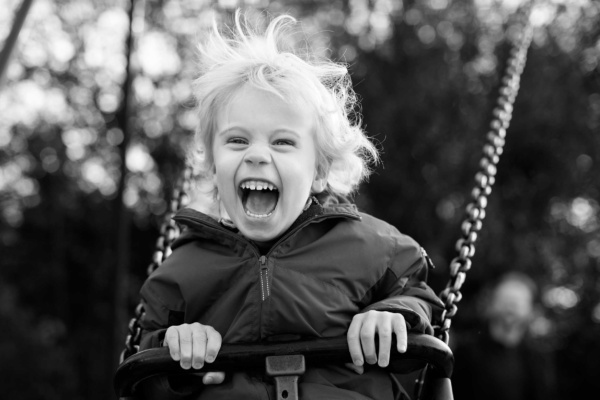 A child laughs with delight on a swing during a London vacation portrait shoot.