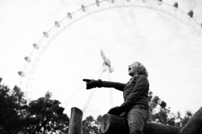 A child sits on playground equipment in front of London Eye.