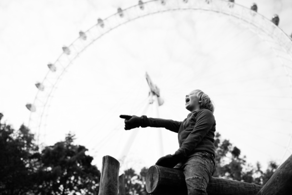 A child sits on playground equipment in front of London Eye.