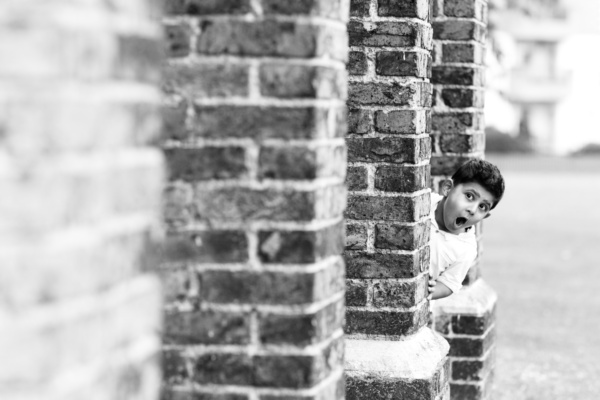 A boy looks around brick columns.