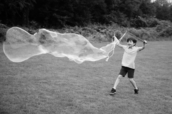 A boy creates a giant bubble in a field.