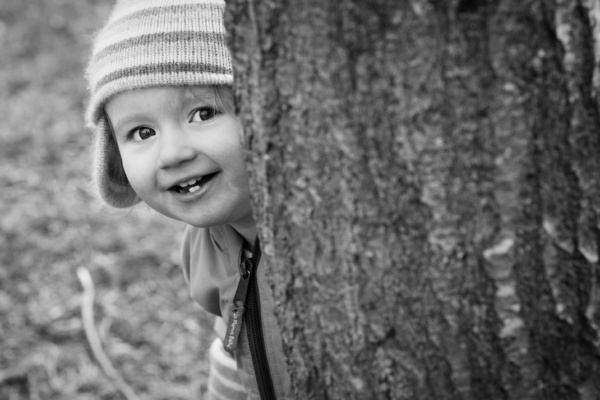 A child wearing a knitted hat peeks around a tree.