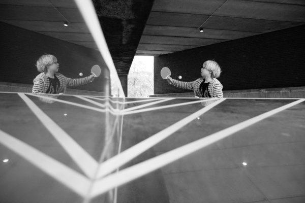 Child plays ping pong with reflection.