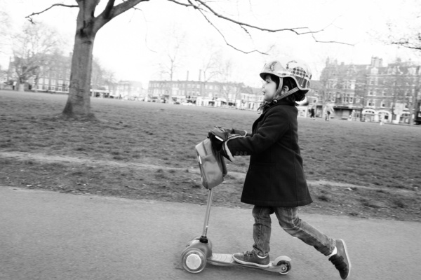 A child rides a scooter along a path through a London park.