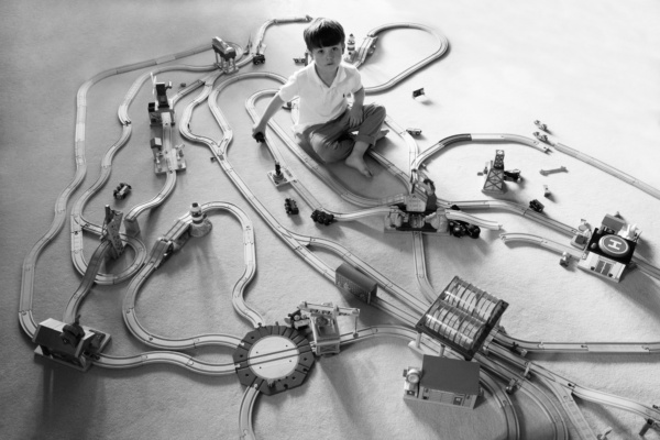 A child sets up wooden train tracks.