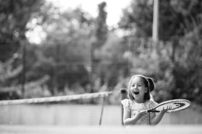 A girl holding a tennis racquet smiles after a game.