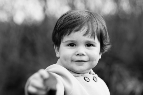 A child smiles and points at the camera in a family shoot.