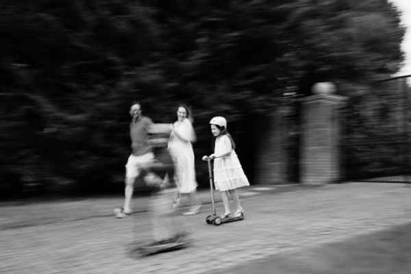 Children on scooters race along a gravel path while their parents run alongside.