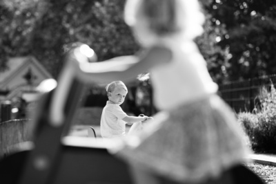 Children ride toys through a garden in the sunshine.