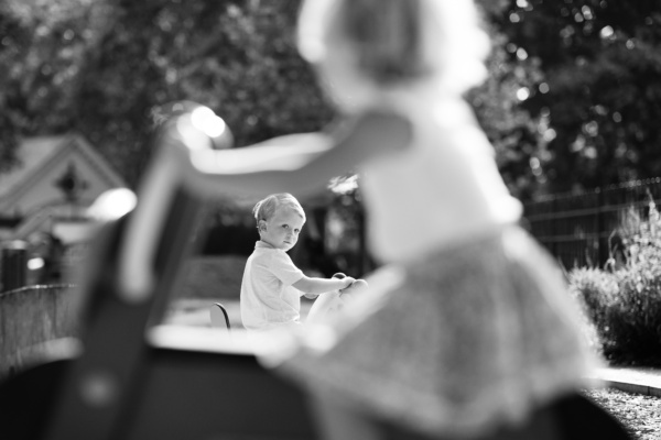 Children ride toys through a garden in the sunshine.