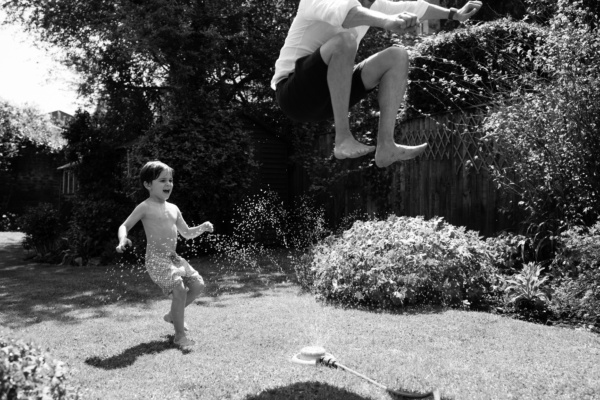 Two siblings run through water sprinklers in the summer.