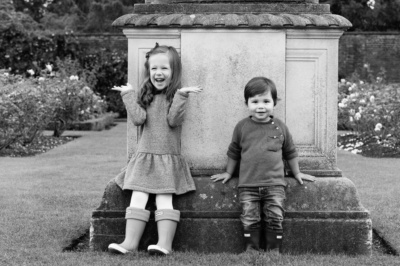 A brother and sister pose for portraits in a formal rose garden.