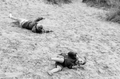 Children roll down a sandbank at the beach.