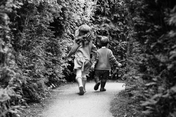 A brother and sister run down a garden path together.