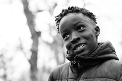 A child's black and white portrait in a park with bare trees.