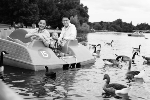 Parents and their toddler feed geese from a paddleboat on a London lake.