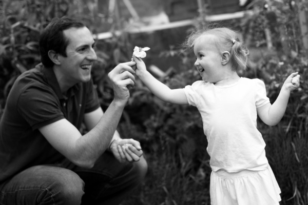 A father and daughter share a flower.