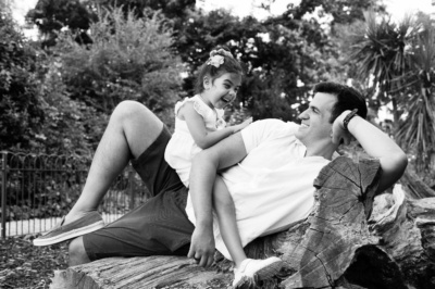 A daughter sits on her father, resting on a felled log.