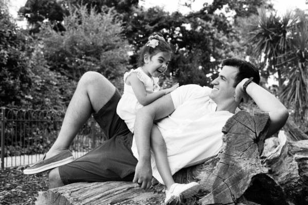 A daughter sits on her father, resting on a felled log.