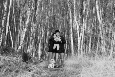 A family and their dog pose together for a black and white family portrait against silver birch.