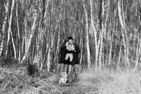 A family and their dog pose together for a black and white family portrait against silver birch.