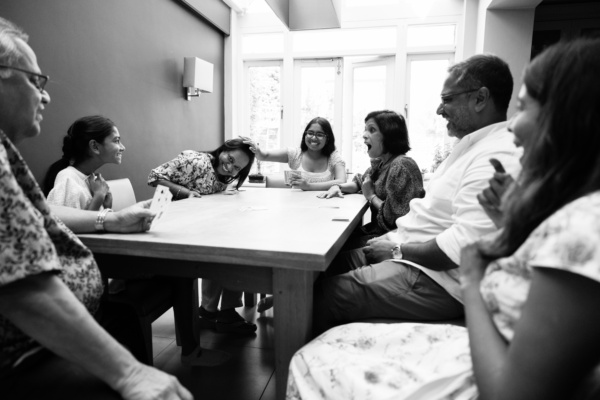 Family generations laugh together around a large table while playing cards.