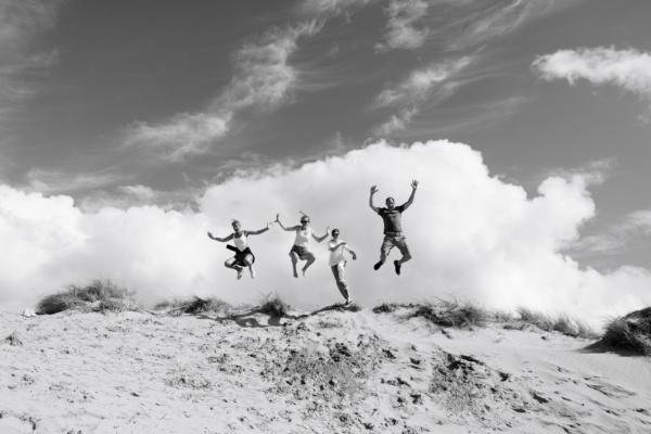 Family jumps off sand dune together.