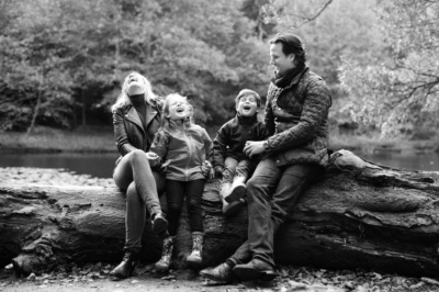 A family sitting on a fallen tree laugh together as part of a portrait sitting by London photographer Helen Bartlett.