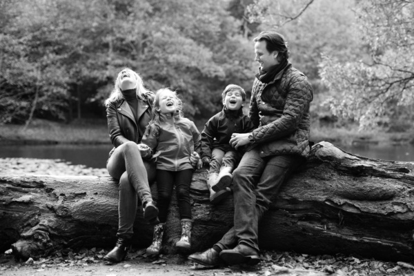 A family sitting on a fallen tree laugh together as part of a portrait sitting by London photographer Helen Bartlett.