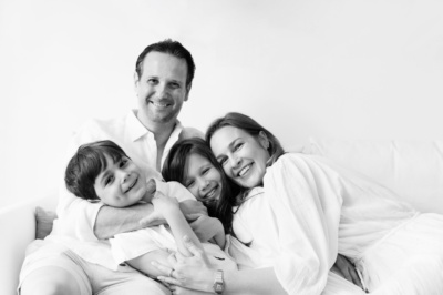 A family of four laugh together on a bed.