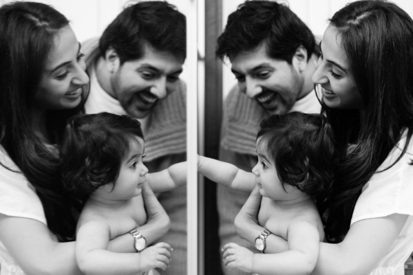 Parents and their baby laugh at their reflections in a mirror, as part of a family shoot.