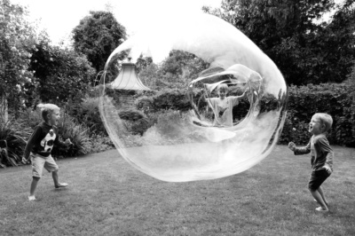 Three children make a giant bubble in the garden.