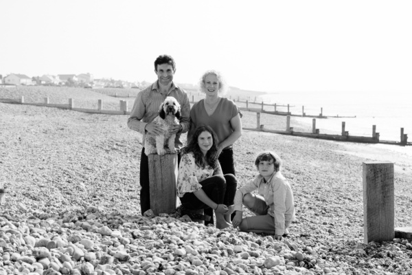 A family portrait with a dog on a shingle beach.