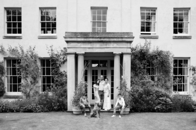 A family with teenagers and a dog pose for a portrait in front of their home.