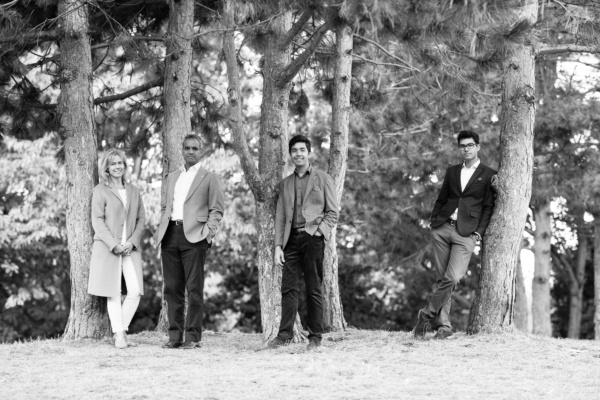 A family with teenagers stand in a group of trees.