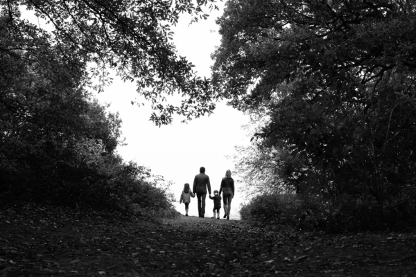 A family walks through a clearing in trees, silhouetting them against the sky.