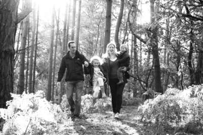 A family walks through sunlit woods, holding hands.