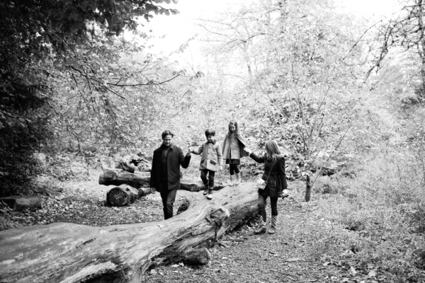 A family walks through the woods with the children walking along a fallen log.